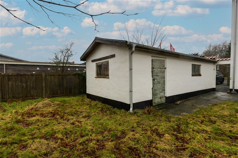 En hvid og sort hytte i en have med græsplæne og en parkeringsplads med en parkeret bil