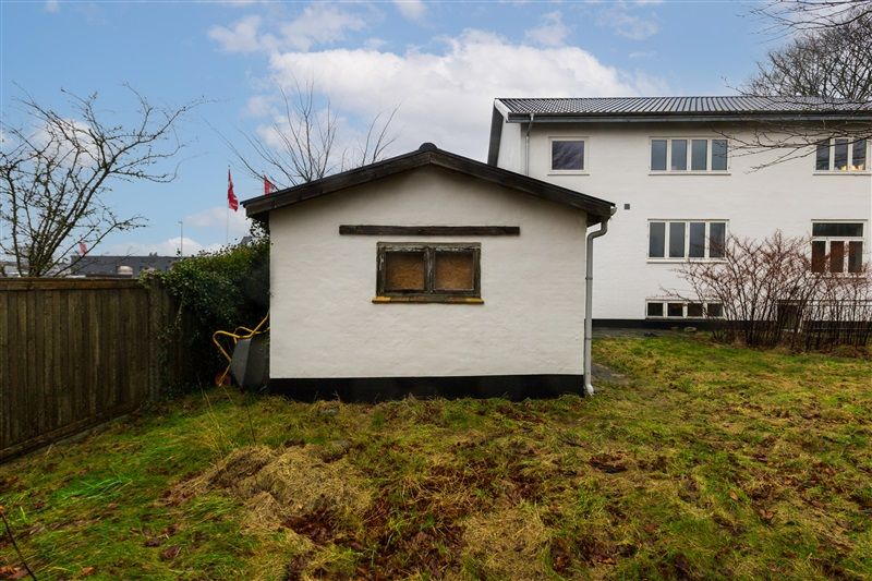 Et hus med rødt flag udenfor og en stor have med græs og træer i baggrunden