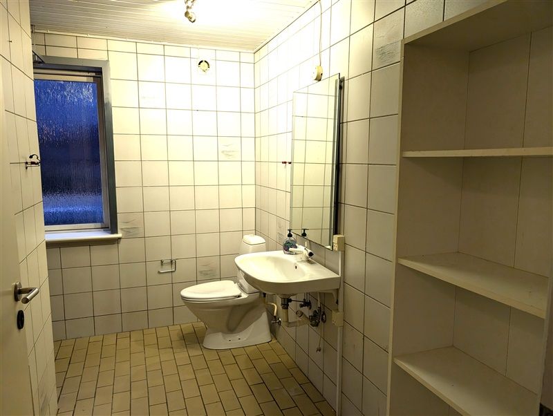 Toilet med toilet, hvidt toilet, hvid vask og spejl samt toiletpapirhylde og håndsæbeflaske