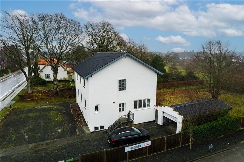 Vejlevej 14 er en hvid villa med en lukket garage og en sort stationcar parkeret foran indgangen