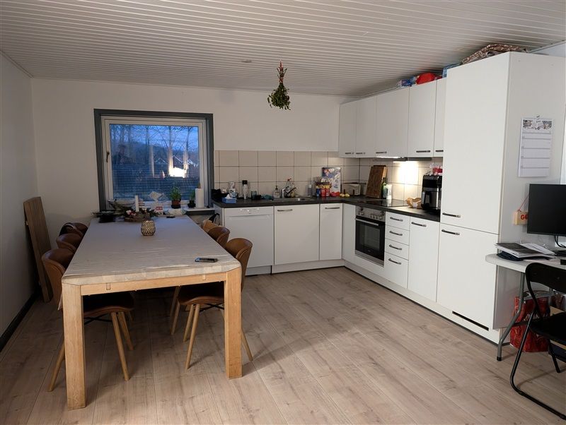 En moderne køkken med hvide skabe, lysegult gulv og massivt træbord med stole omkring