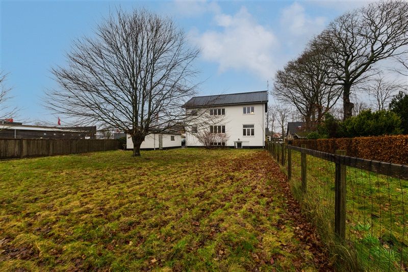 Det er et lyst og rummeligt hus med terrasse, der er omgivet af grønne græsflader og en lav hegn