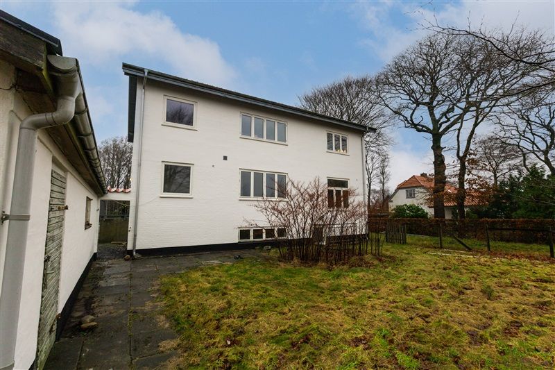 En hvid toetages bygning med flere vinduer og en række buske i forgrunden