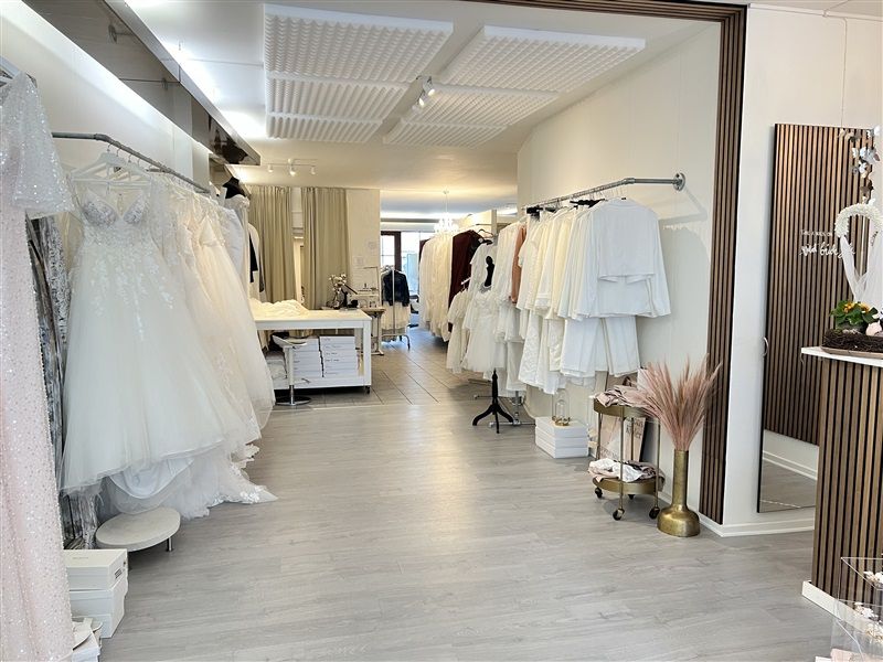 I en luksuriøs brudekjolesal står flere brudekjoler opstillet i rækker og smukke buketter i vaser