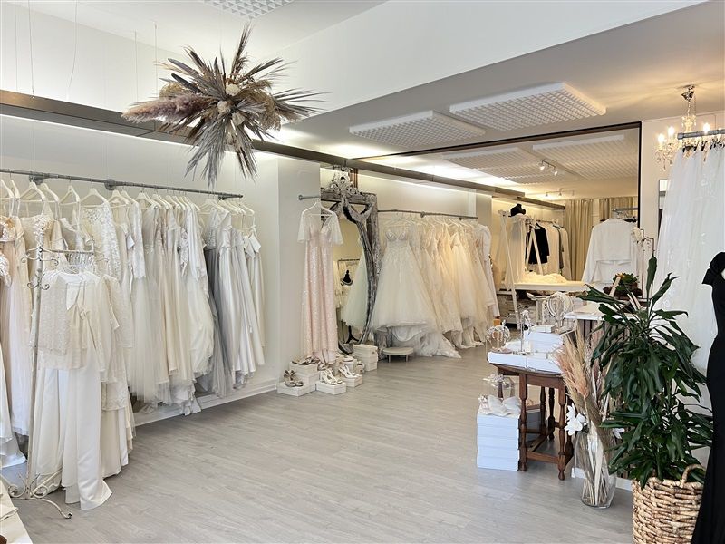 En butik med ægteskabskjoler, hvor der er et højt loft med hængende kranse og et stort spejl med kjoler på