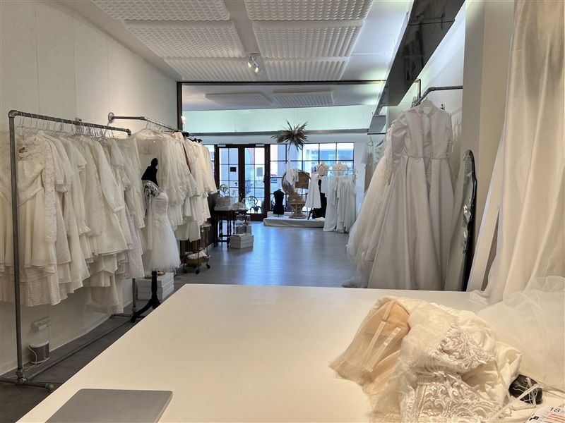 Bryllupskjoler i hvidt hænger på stålebøjler i et rum med hvide vægge og loft. Kjolerne er foldet og pakket i plastik.