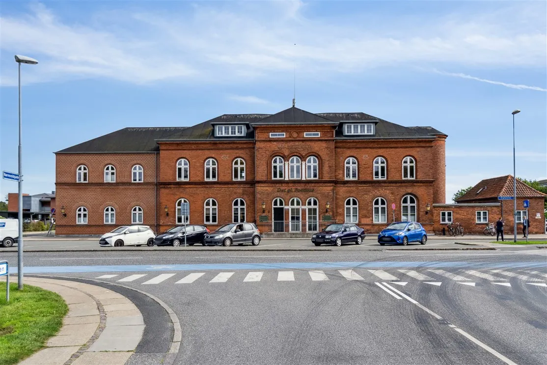 En stor bygning med røde mursten og mange vinduer parkeret med fem biler foran Nyborgs posthus