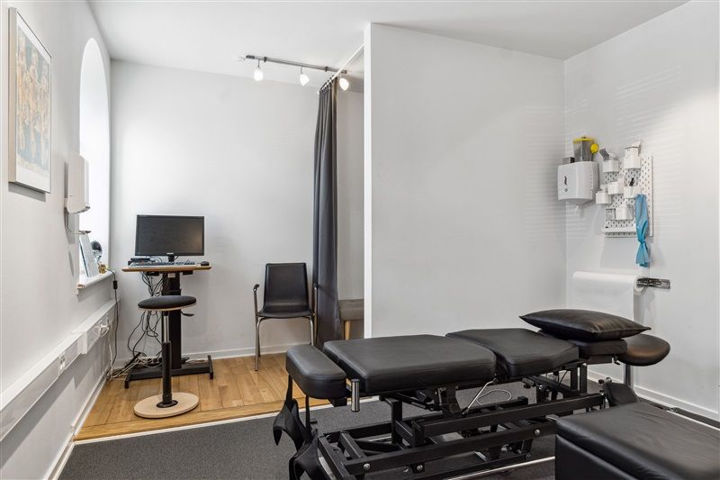 Et værelse med to massagebord, en computer og en stol samt et bord med en skærm og et kamera