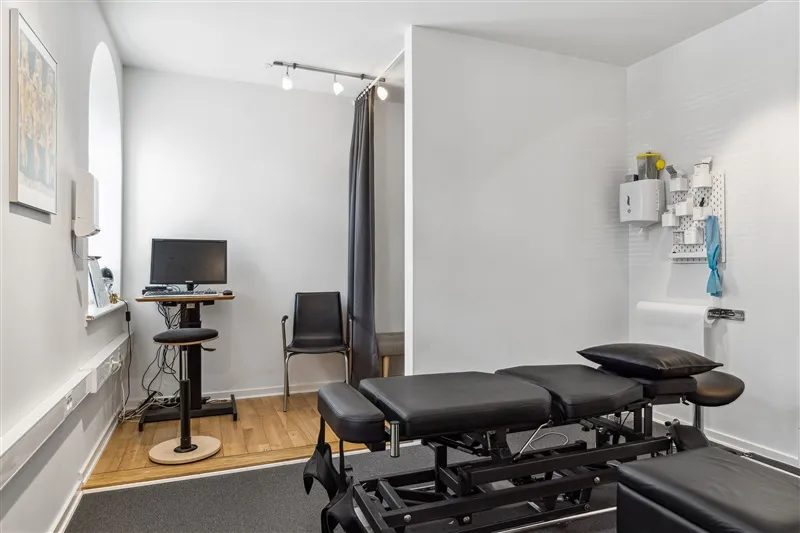 Et værelse med to massagebord, en computer og en stol samt et bord med en skærm og et kamera