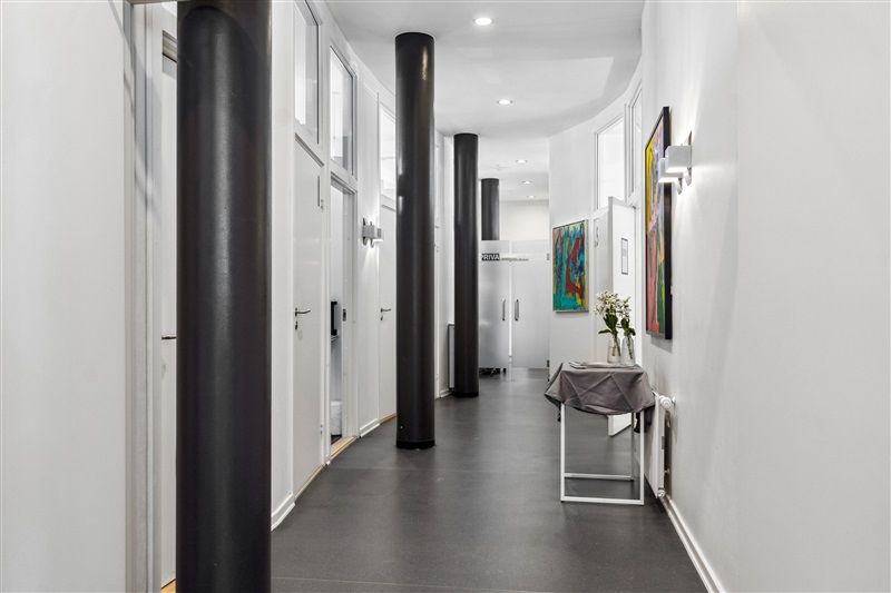 Kort korridor med slanke søjler og moderne indretning, møbler og kunstværker på væggen