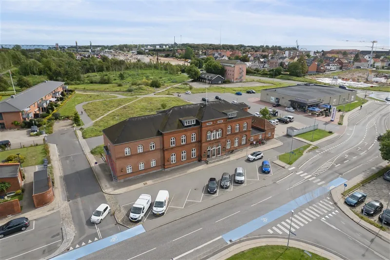 Erhvervsejendom med mange parkeringspladser og biler og grønne arealer og bygninger i baggrunden