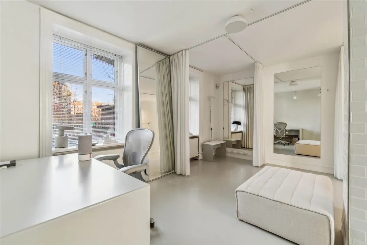 Minimalistisk og stilren kontor med hvidt bord, stol og høj garderobespejl med valkur og vinduer med solblinde