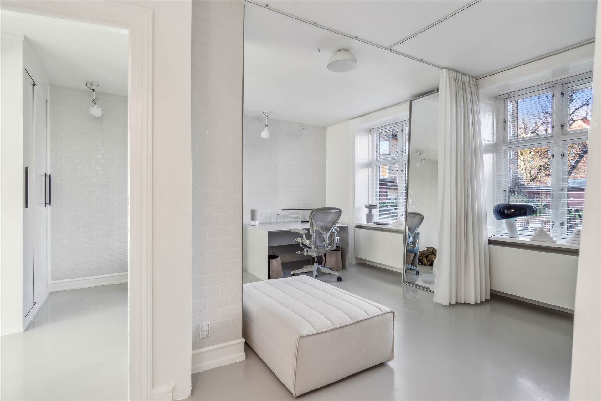 Hjørnekontor med højt spejl og store vinduer i moderne interiør med hvidt og gråt gulv og hvide vægge