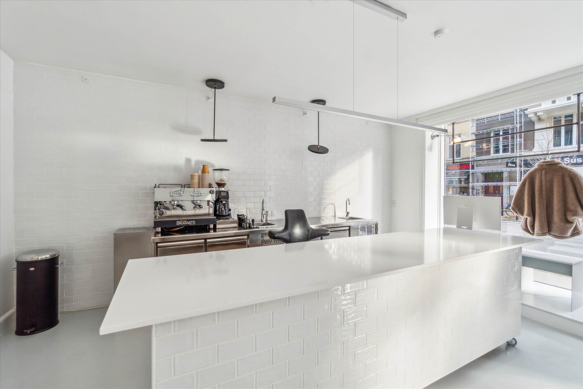 En hvidklædt køkken med en stor ø i midten, kaffemaskine og en hængende lampe