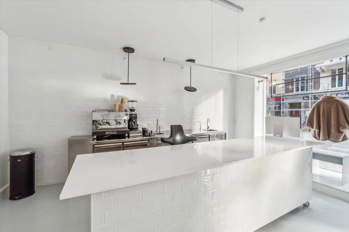 En hvidklædt køkken med en stor ø i midten, kaffemaskine og en hængende lampe