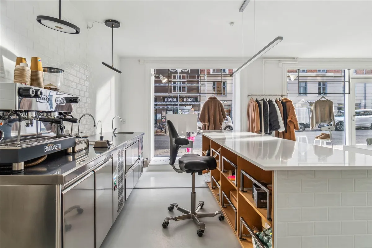 Kaffemaskine med kopper, stol og udstilling af tøj i københavner-butik med høj fodgængertrafik og glasdøre og vinduer