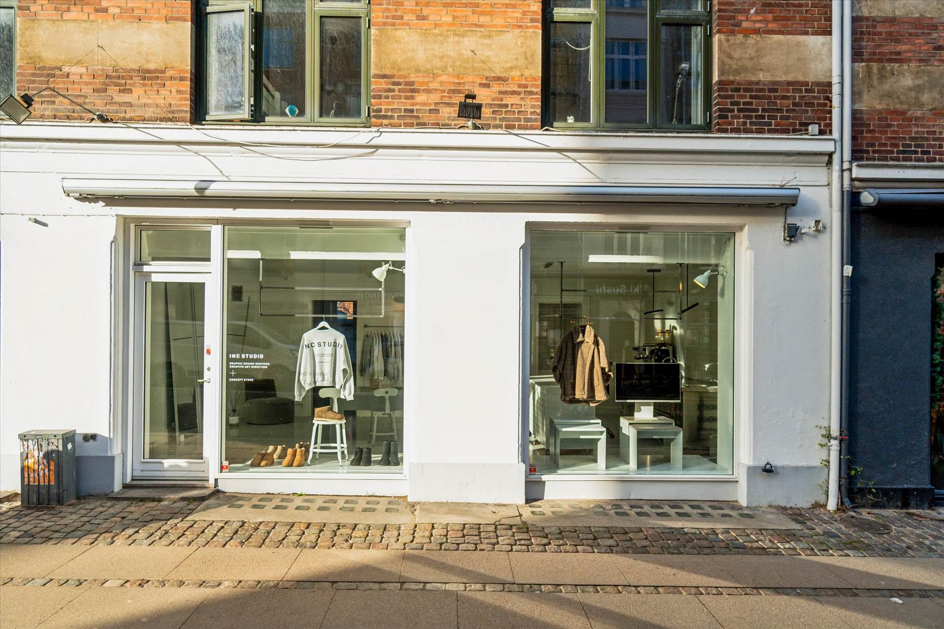 Butik med glasvinduer og tøj i udsigten, mærke navn Inc Studio, stol med håndklæde og sko i udstillingen, og en stol og