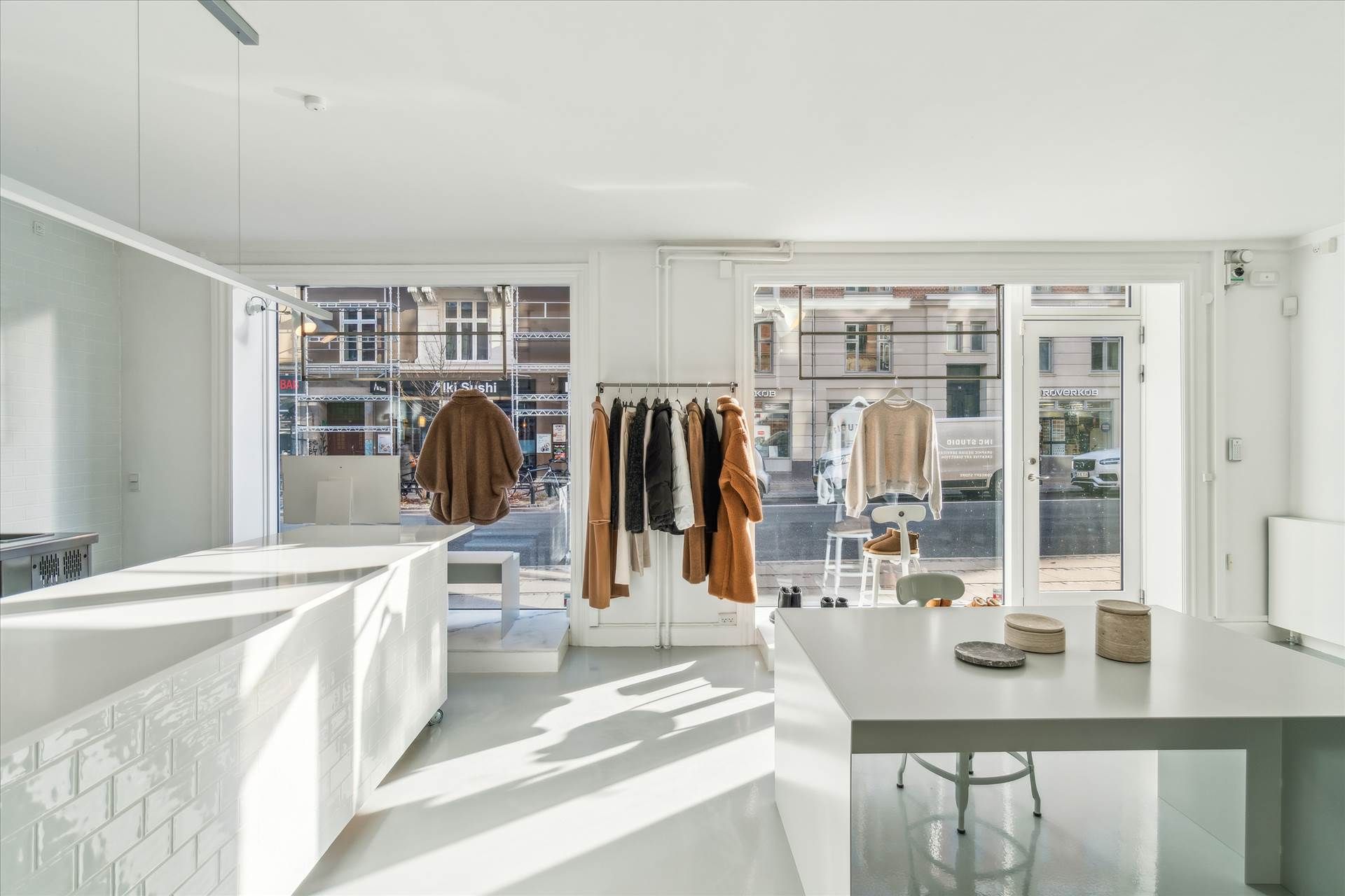 En minimalistisk hvid interiør med højloftede og hvide vægge, fuld af møbler og tøj, sammen med lyse og reflekterende