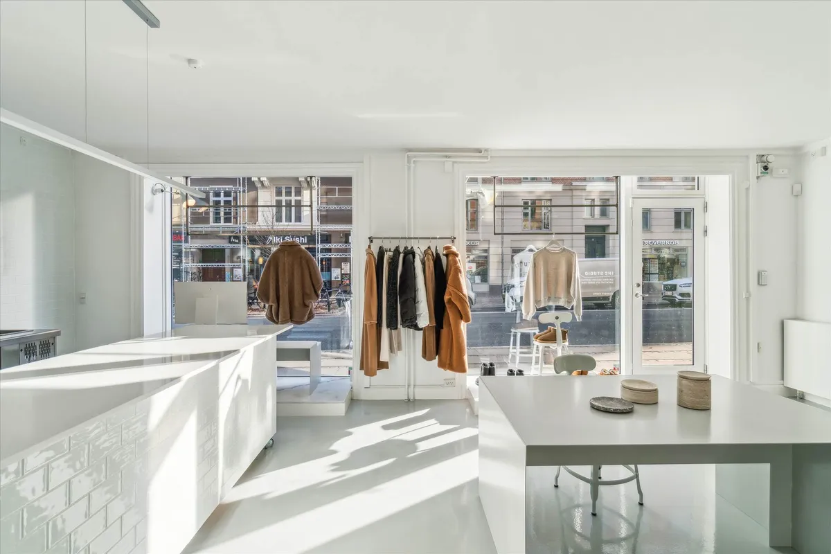 En minimalistisk hvid interiør med højloftede og hvide vægge, fuld af møbler og tøj, sammen med lyse og reflekterende