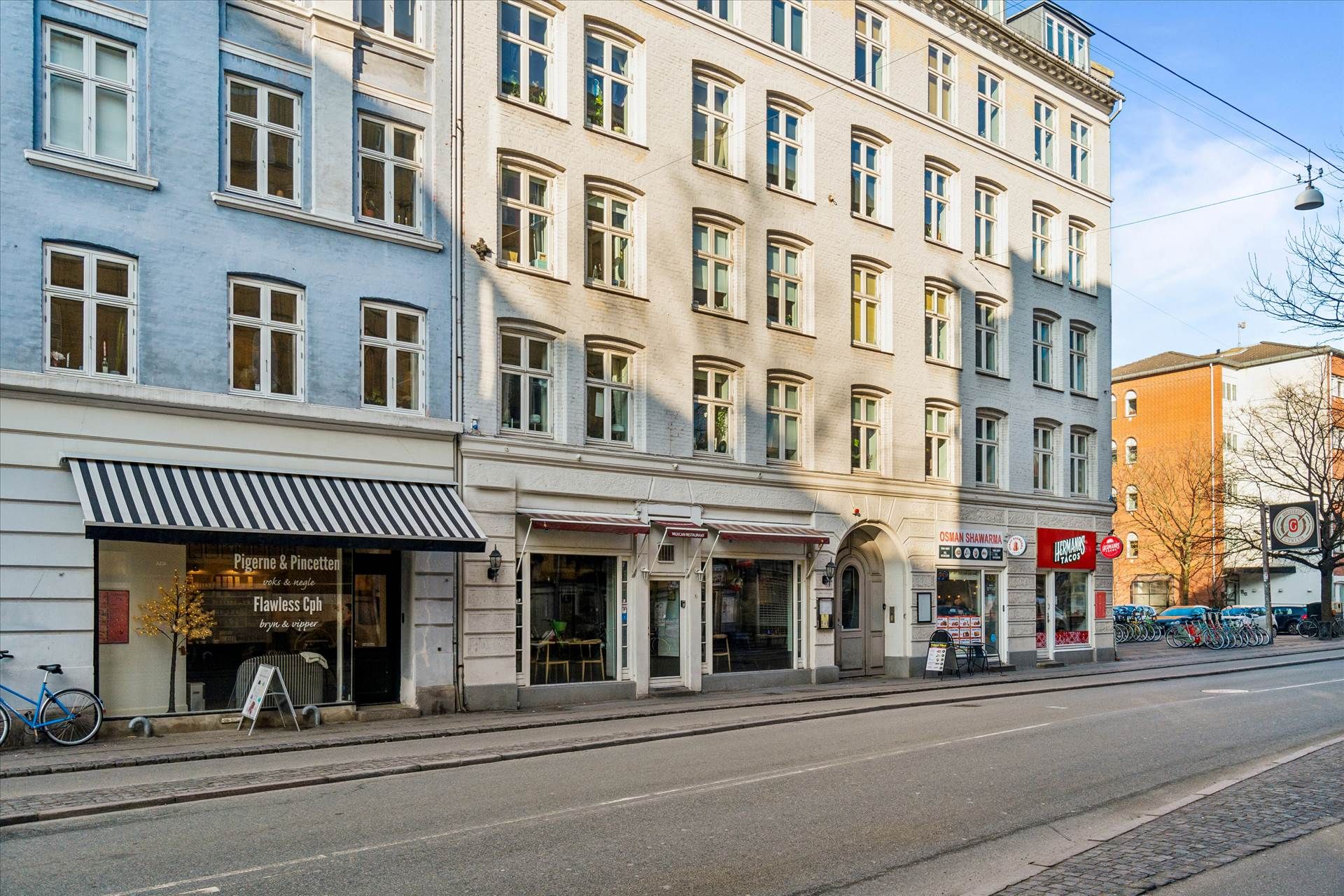 To etager højt erhvervsbygning med mange vinduer og tre butikker med udstillinger og udsalgsmærker