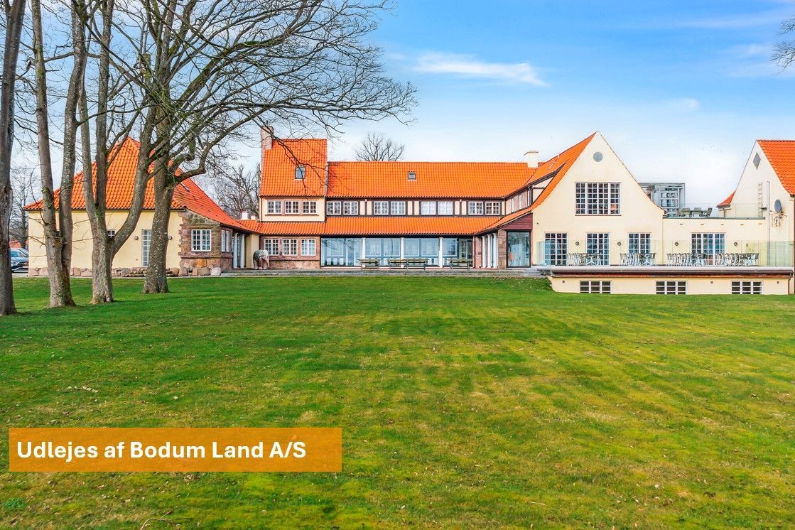 Elegant hus med orange tag og glasvinduer står i fredfyldt park med græsplæne og træer