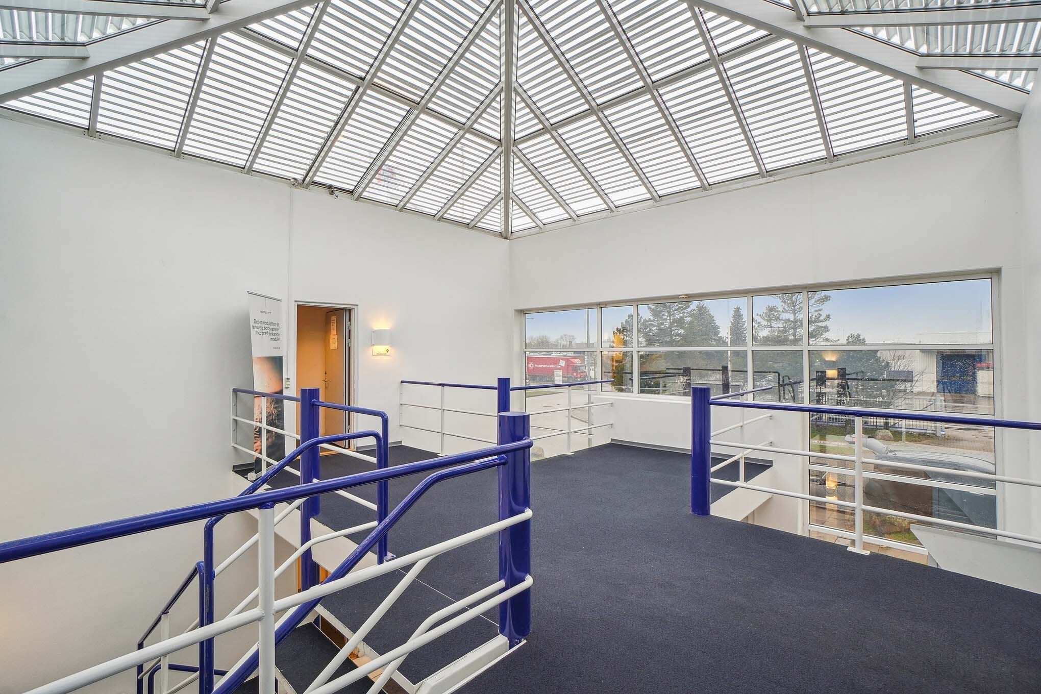 Indre område med moderne loftskonstruktion og glasvinduer samt slanke stålrækværk på balkoner og trapper.