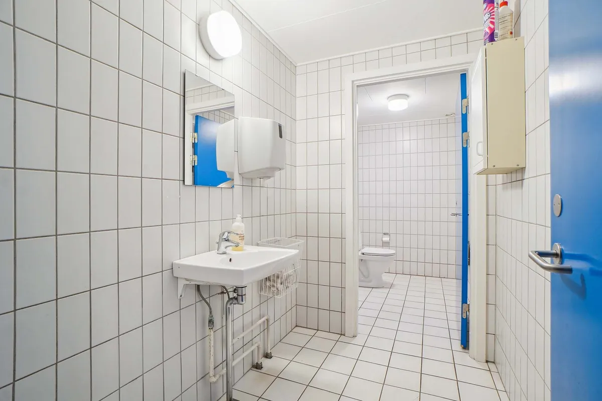 En rent vask og toiletrum med en hvid vask og en håndklædeholder, samt en hvid toiletbøsse.