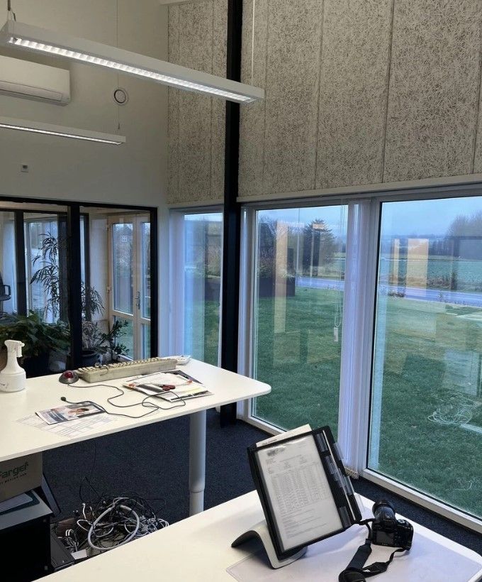 Kontorlokaler med moderne møbler og en stor vinduesfront med udsigt til græsarealer. Værelse med to hvide skriveborde og