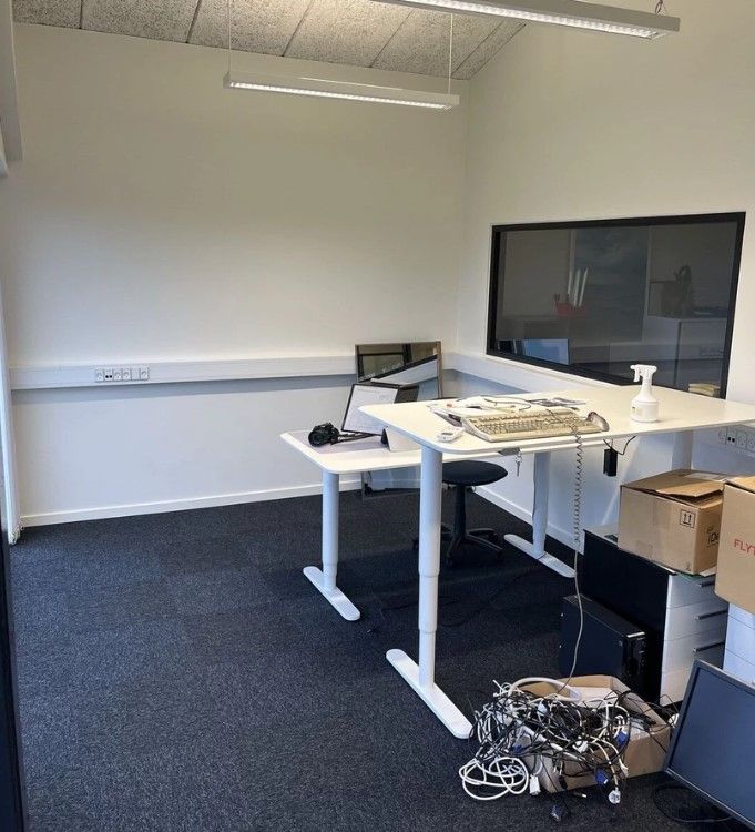 Kontor med høj gulvdekoration og to skriveborde med flere computere og en stor skærm samt en kasse med kable