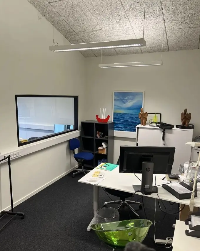 Kontorlokaler med lyse loftsbelægninger og en skrivebord med en HP-computer og en skrivemaskine