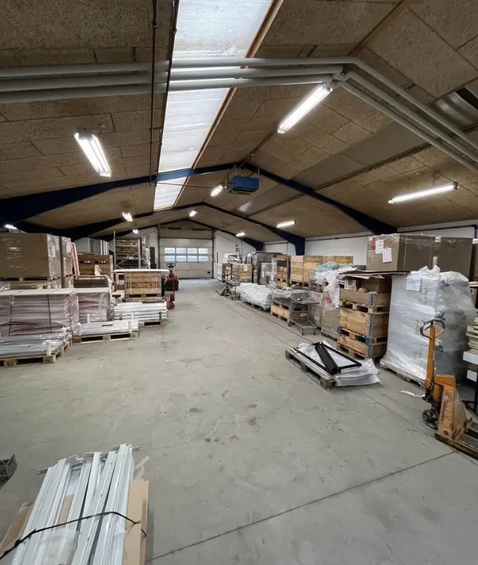 Lager med lagerhylder og kasserne, vinduer og døre, samt gulv og loft, forsynet med lysekroner og ventiler