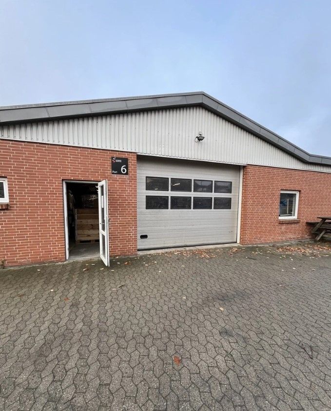 En stor, nybygget, rød murstensbygning med garagedør og to vinduer, der udgør en del af en række kontorlokaler