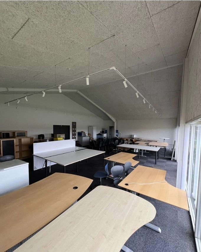 Kontor med højloft, mange skriveborde og stole samt flere stolpeborde med skarpe linjer
