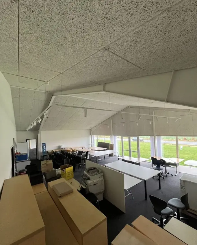Kontorlokaler med flere skriveborde, stolpe, stole og bokse samt et skanneri og printer. Højt hvælvet loft og store vinduer.