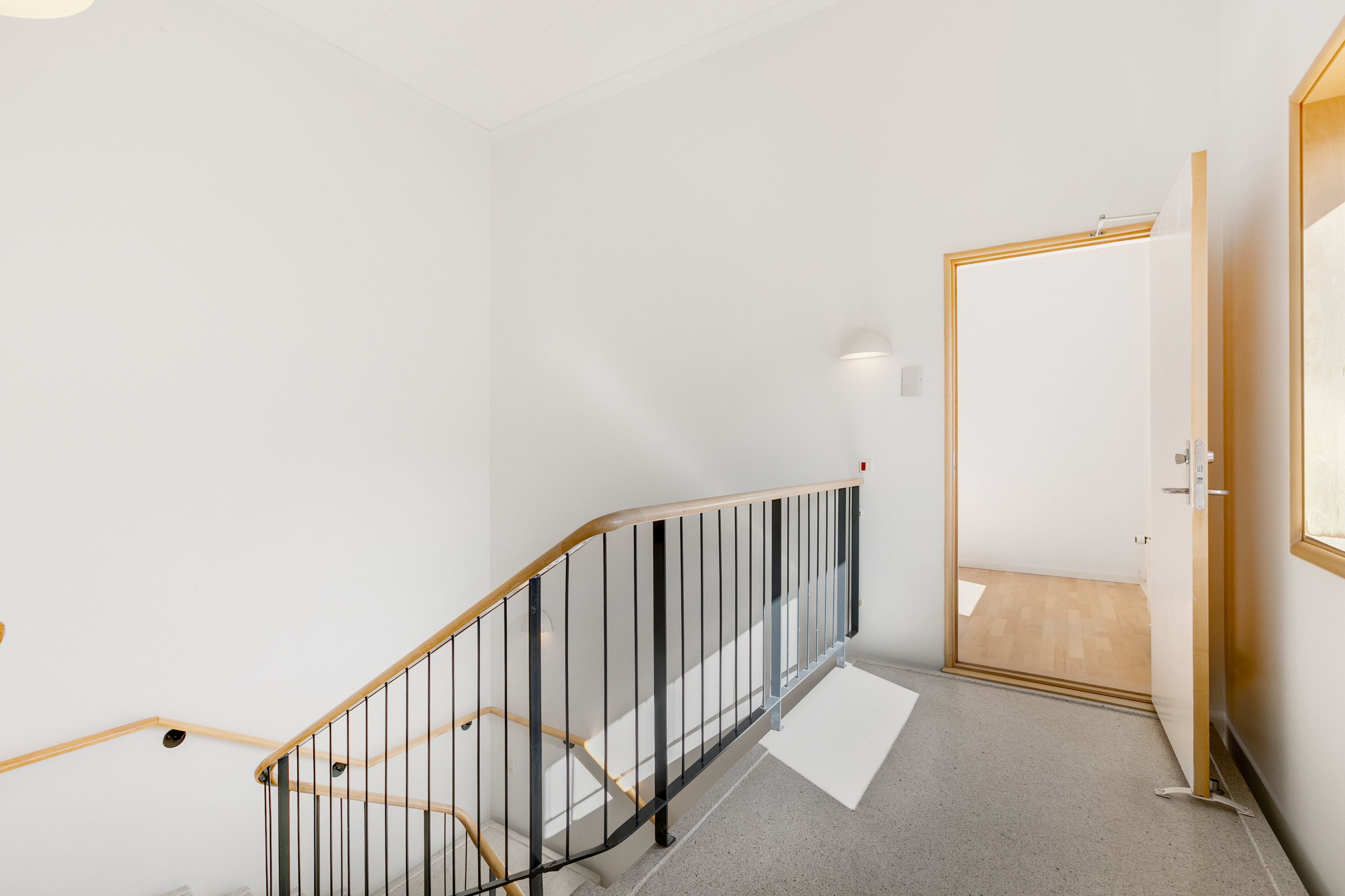 Åben dør til et moderne lejlighedshus med lyse vægge, hvidt gulv og moderne trappe med slank stål og trædesign og en slank