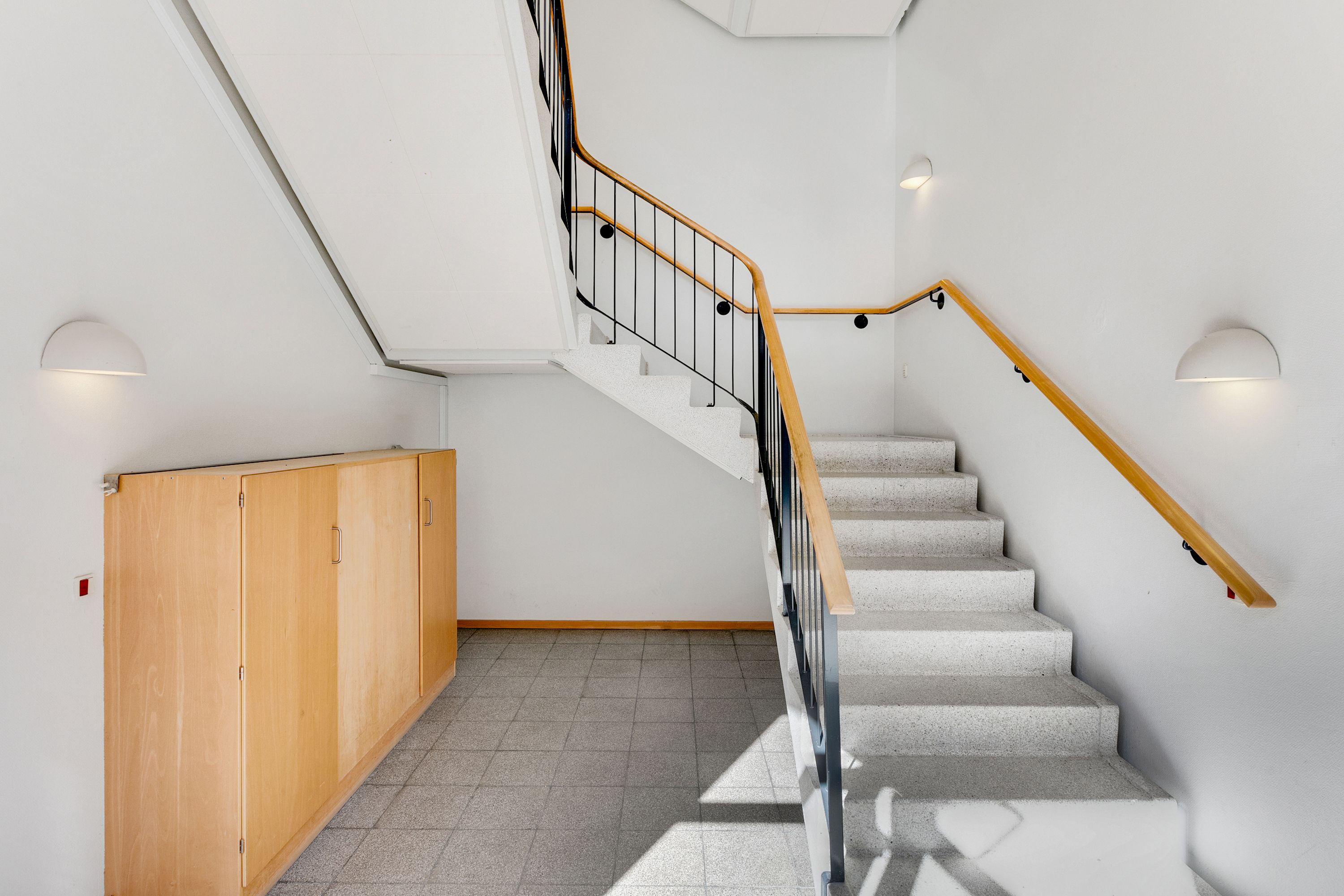 Lyst kontor med lysegrå gulvfliser, hvidt gulv og vægge samt marmorstige med møbler og lysekroner på væggen