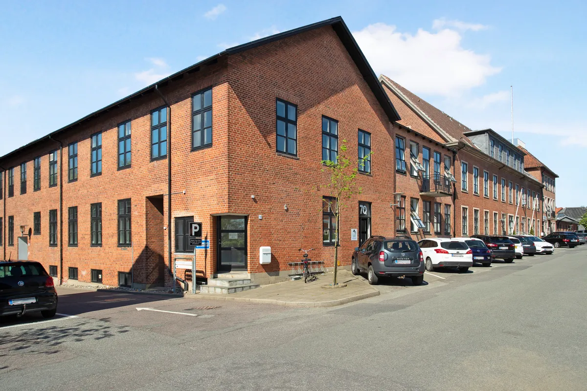 En stor bygning med røde mursten og glasruder parkeret biler foran og et skilt med bogstavet P