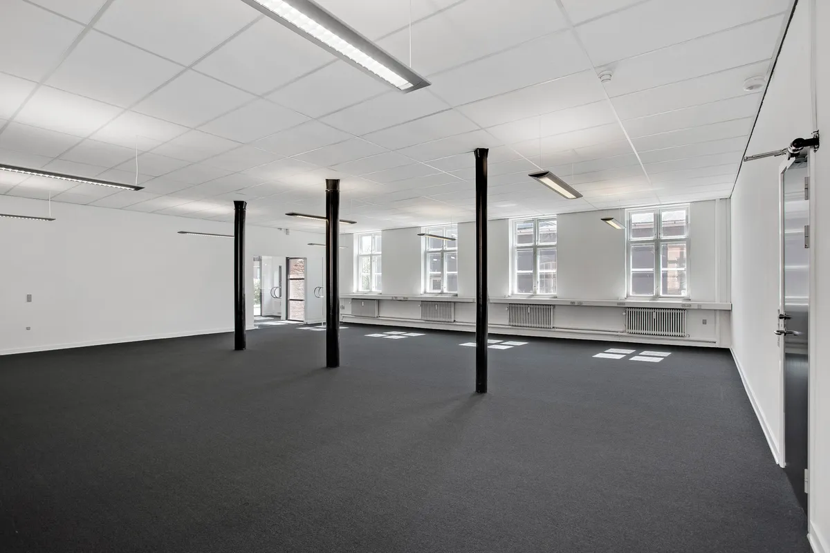 En stor, lys, og tom erhvervslejemål med lyse lofter og gulv og flere vinduer og radiatorer