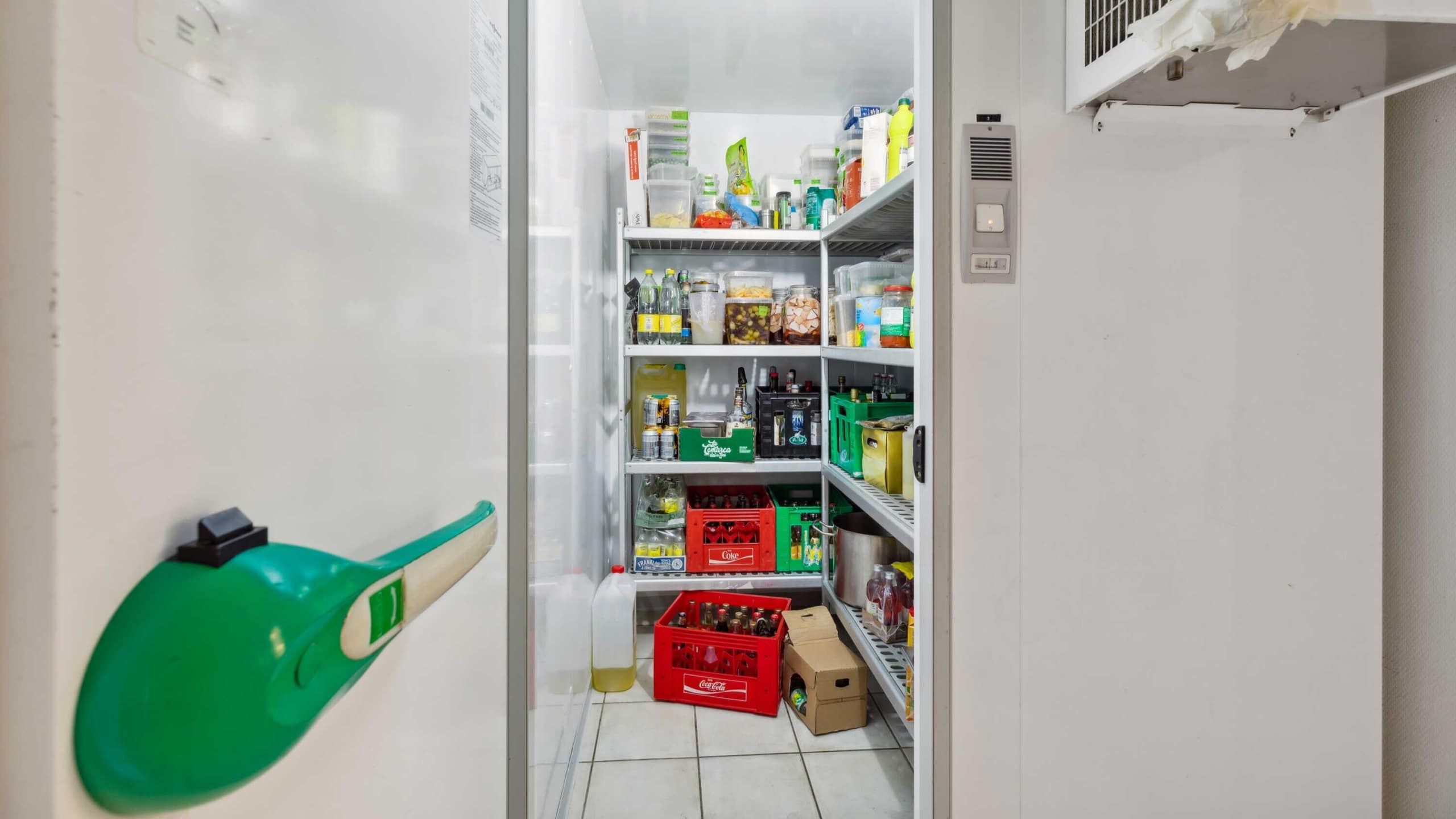 En køleskab med flere hylder, indeholder forskellige varer som drikkevarer, snacks, krydderier og emballage