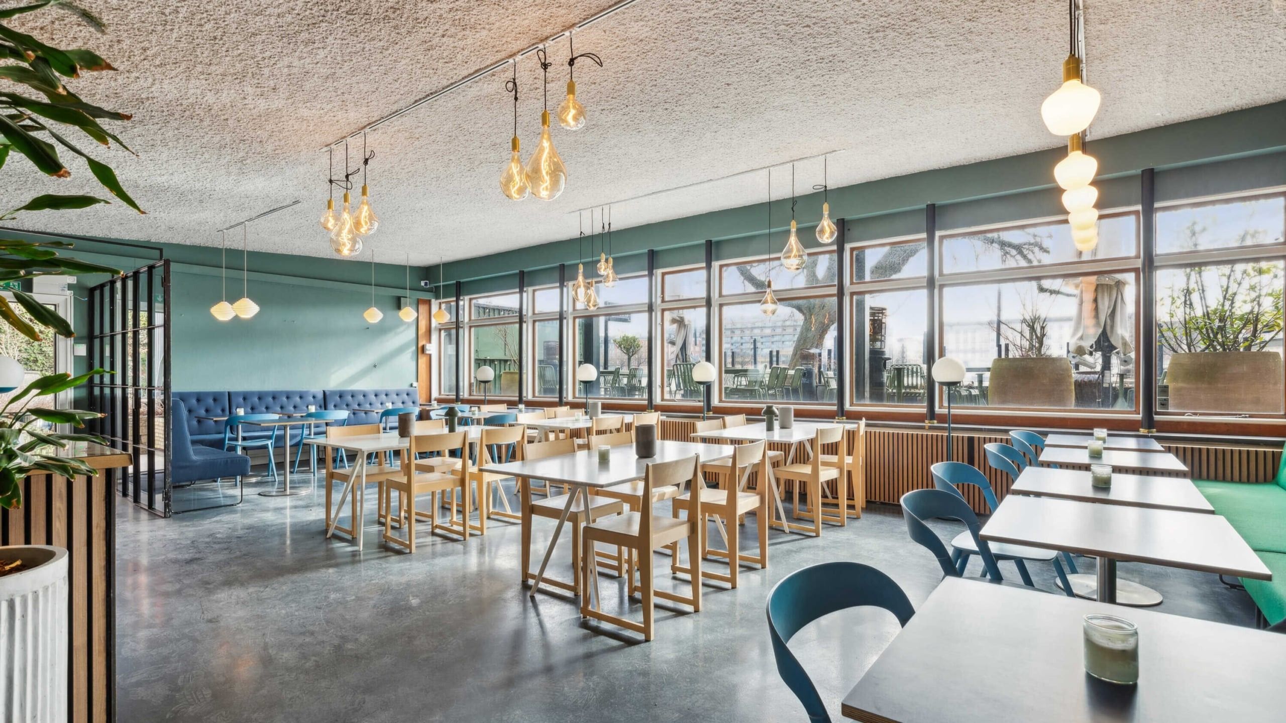 En moderne cafe med lyse grønne vægge, store vinduer og en mængde bord og stole med en dejlig udsigt til byen