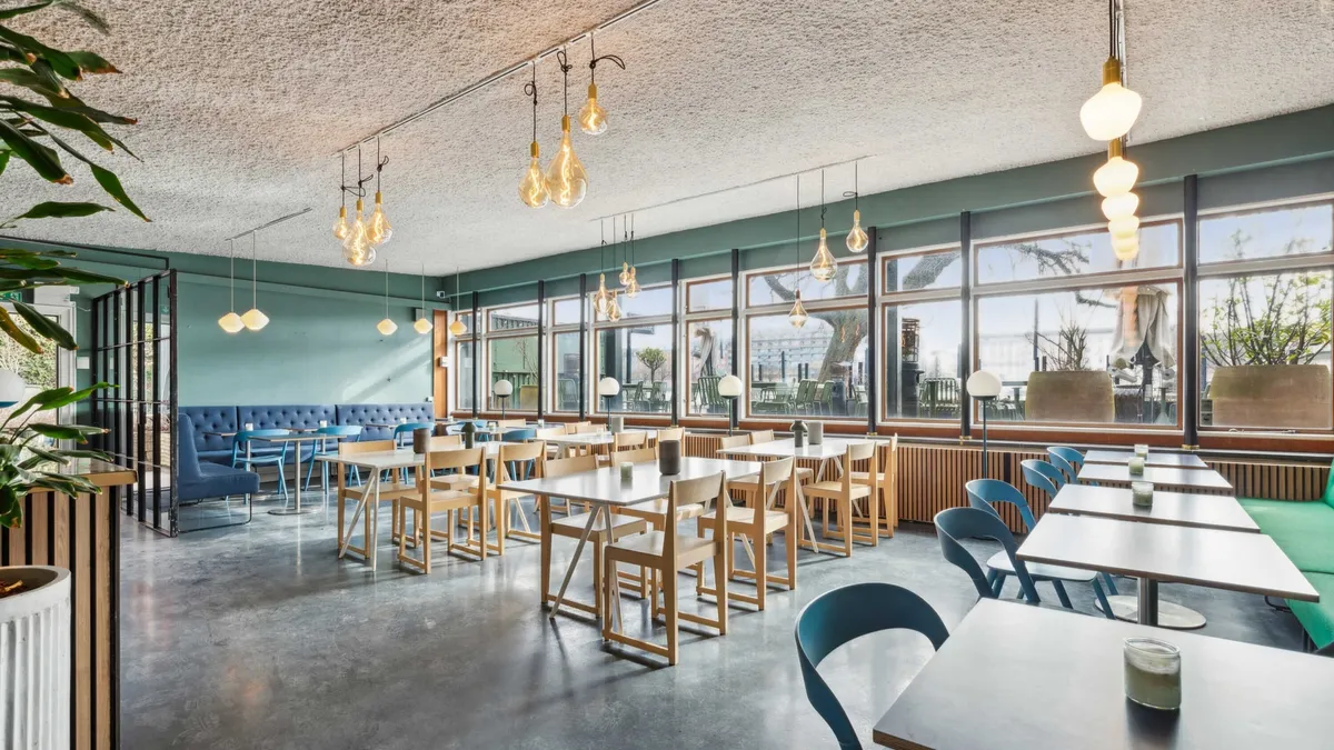 En moderne cafe med lyse grønne vægge, store vinduer og en mængde bord og stole med en dejlig udsigt til byen