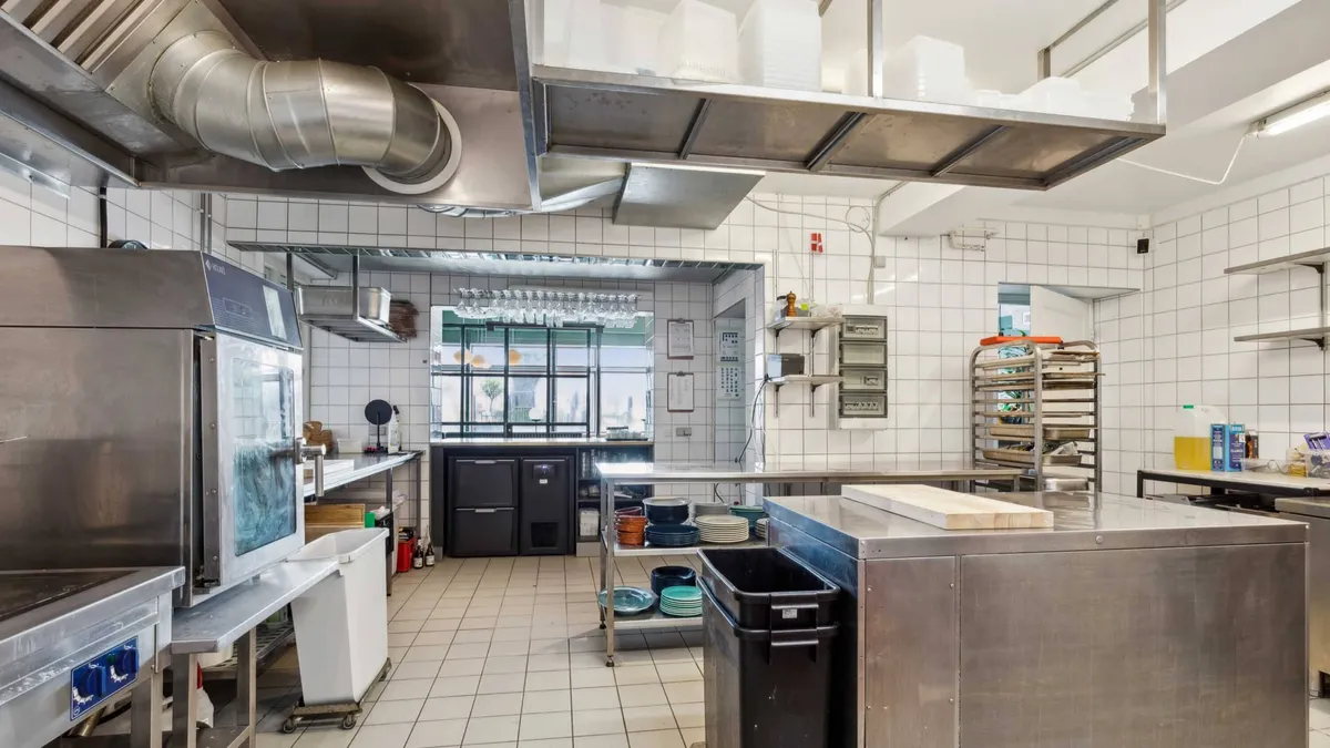 Et moderne køkken med metalapparater og en stålkøkkenbord, hvor der ligger et hvidt skærebræt og en stor skraldespand