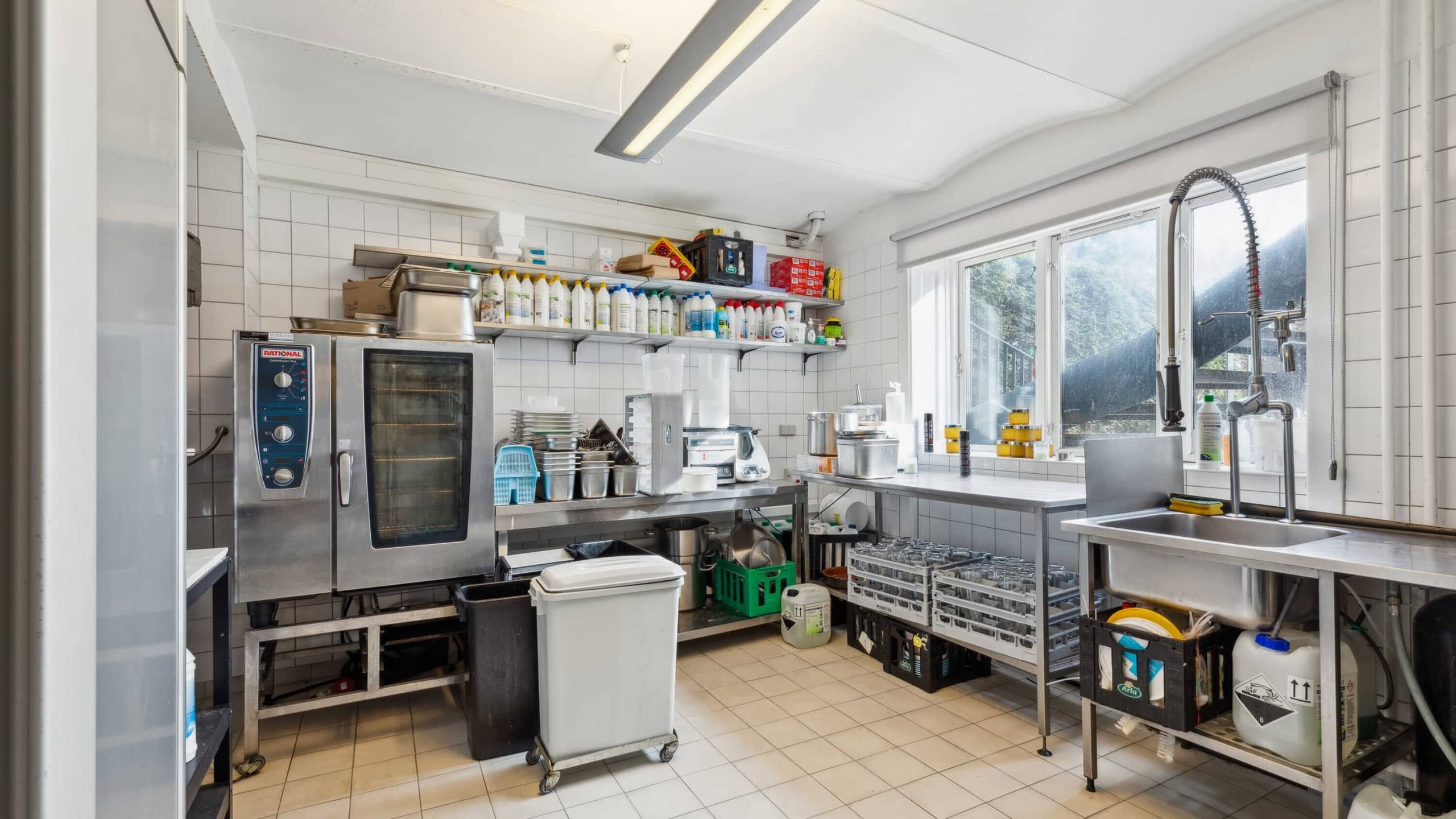 En veludstyret køkken med ovne, et stort arbejdsmæssigt bord, skarpe, rene reoler og en stor, ren vaskebækken