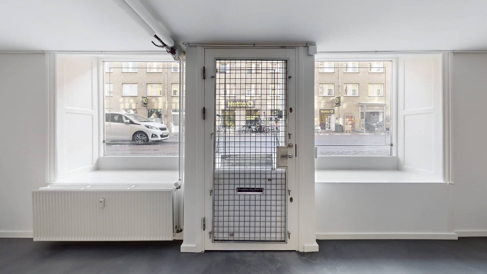 Lejlighed med store vinduer og en hvid dør, der fører ud på gade med biler og bygninger