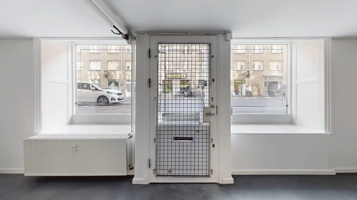 Lejlighed med store vinduer og en hvid dør, der fører ud på gade med biler og bygninger