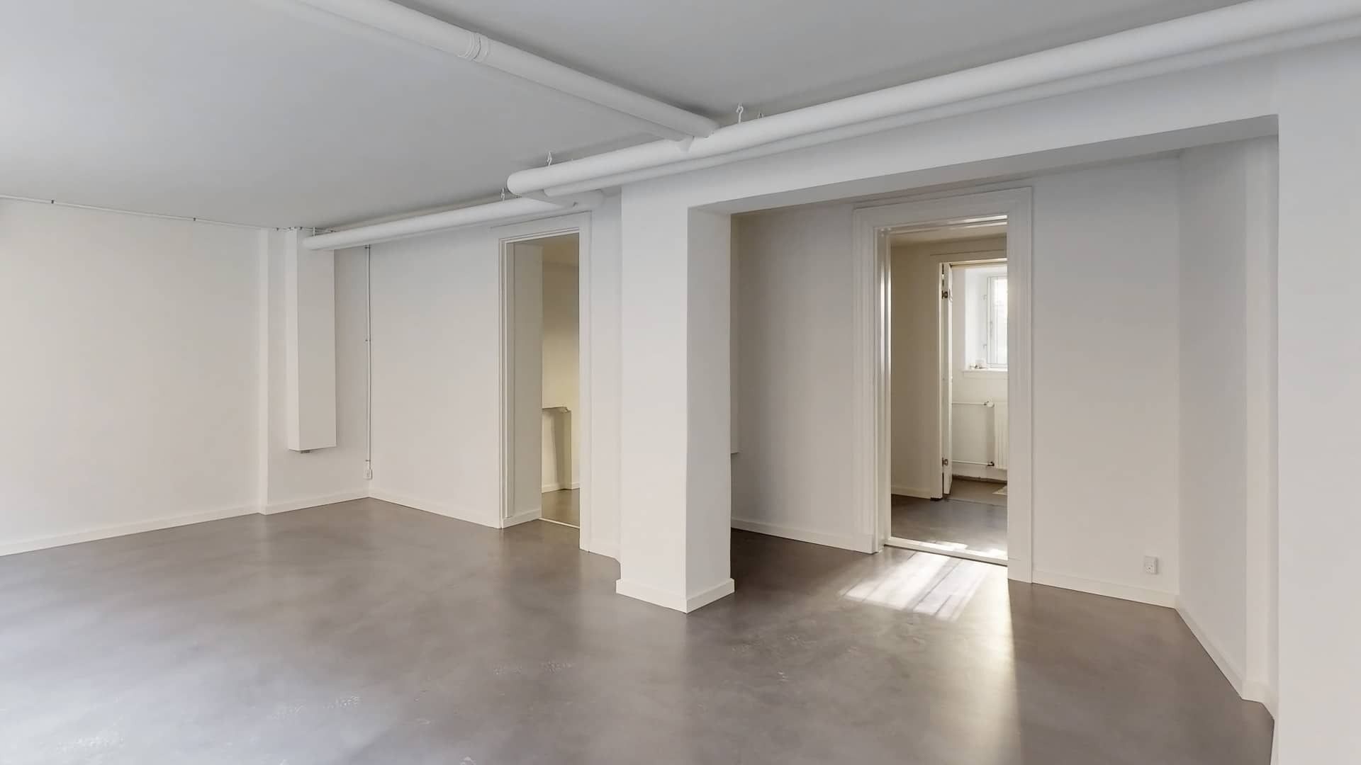 Erhvervslejemål med moderne design, hvide vægge, lysegulve og lysepiper samt to døre i hvide glas.