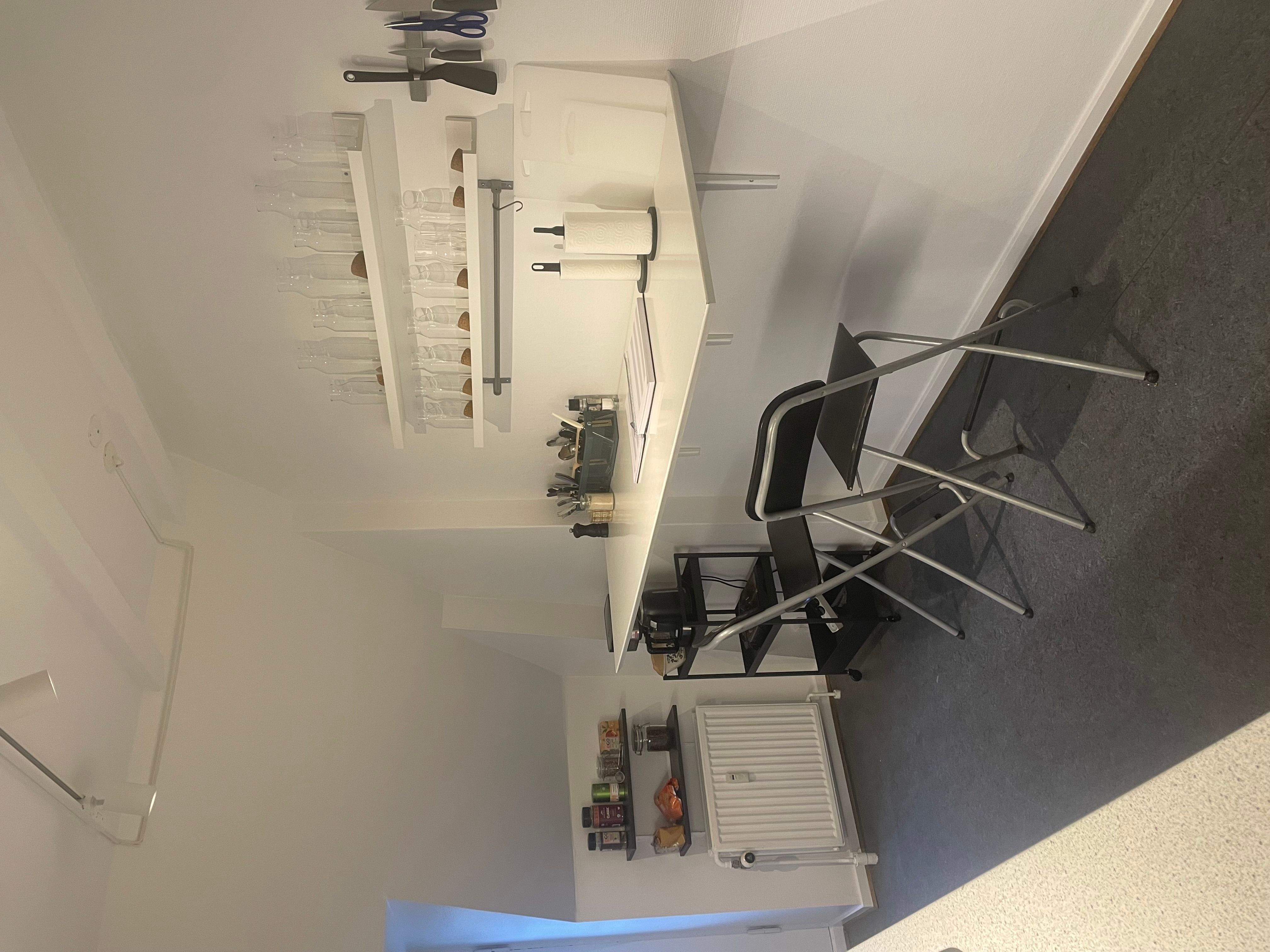 Arbejdsrum med højt loft og loftsvinduer, minimalistisk indretning og møbler inkl. bord, stol, hylde og hængekøkken.