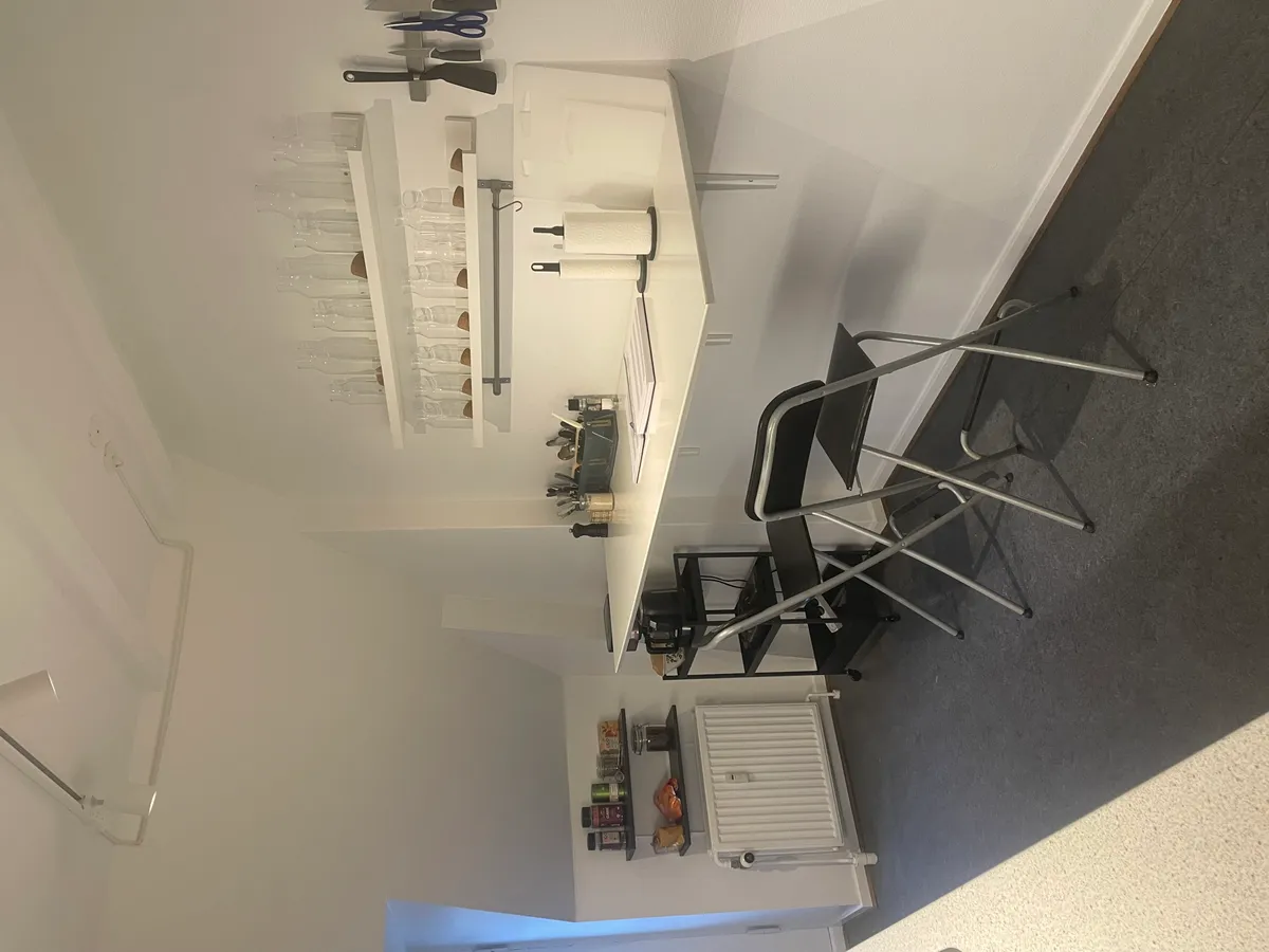 Arbejdsrum med højt loft og loftsvinduer, minimalistisk indretning og møbler inkl. bord, stol, hylde og hængekøkken.