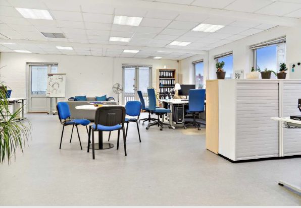 Mødelokale med runde borde og blå stole samt højloftet kontorfællesskab med skriveborde, computere og plantepoter