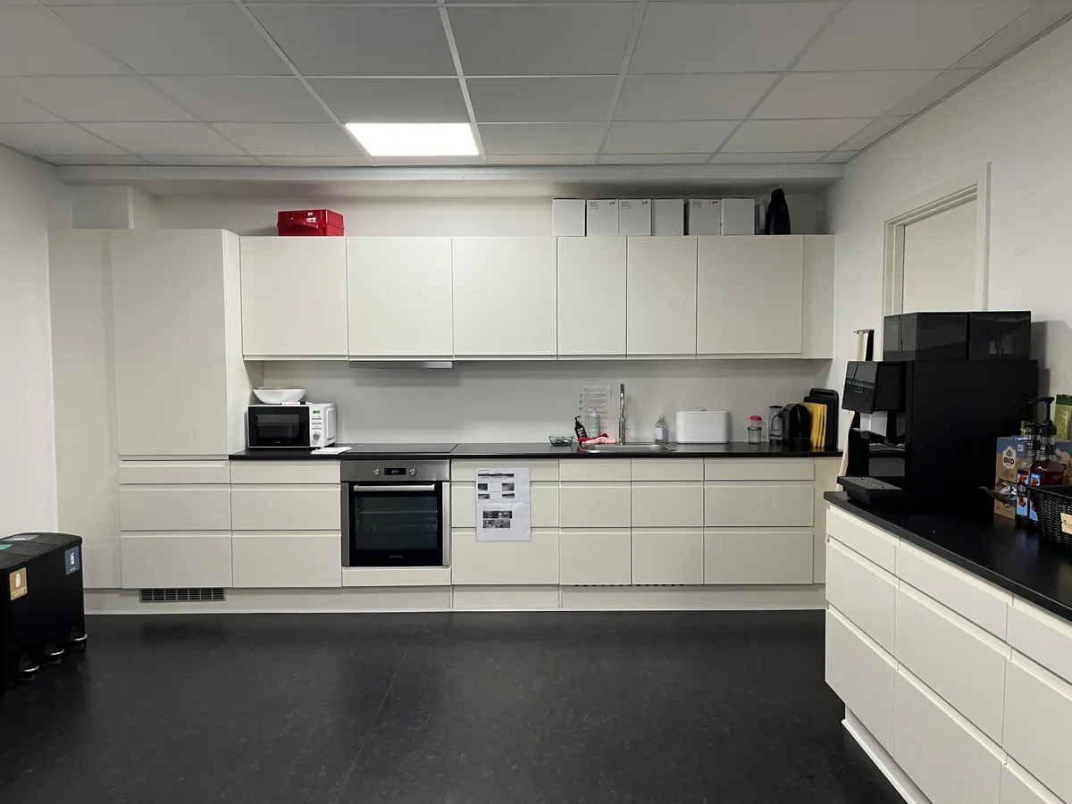 Kontorlejemål med moderne køkken og højloft, hvidt køkken med indbygget ovn og mikroovn, sort kaffemaskine, alle hængende